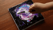 a hand is holding a spatula over a painting