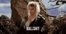 a man with blonde hair is standing in front of a rock with the words bullshit written on it .