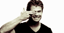 a man in a black shirt is smiling and pointing at his eyes