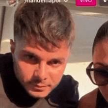 a man and a woman are standing next to each other and looking at the camera . the man is wearing sunglasses .