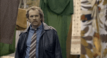 a man in a leather jacket and tie is standing in front of a row of clothes