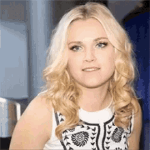 a close up of a woman with blonde hair and blue eyes wearing a white and black dress .