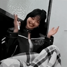 a woman in a black jacket and plaid pants is sitting on a couch with her arms outstretched .