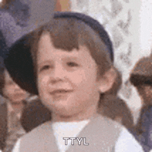 a young boy wearing a hat and a vest is smiling and says ttyl .