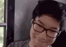a young man wearing glasses is smiling while sitting in front of a window .
