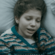 a girl in a blue and brown striped sweater is laying on a bed with the word prime on the bottom right