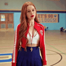 a woman in a red jacket and blue skirt stands in front of a sign that says let 's go sleddogs