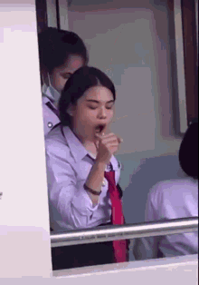 a girl in a white shirt and red tie is coughing in front of a window .