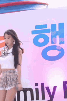 a woman in a plaid skirt is dancing in front of a sign that says mily