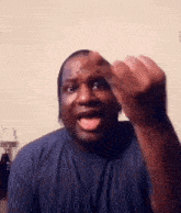 a man in a blue shirt is making a funny face with his hand