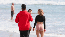 a man in a red hoodie is walking on the beach with two women