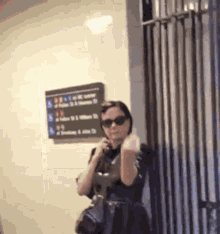 a woman wearing sunglasses and a purse is standing in front of a sign that says ' a ' on it