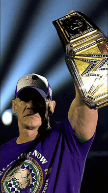 a man wearing a purple shirt that says time now holds a wrestling championship belt