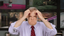 a man in a white shirt and red tie is scratching his head in front of a television .