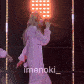 a woman in a pink hoodie is singing into a microphone on stage