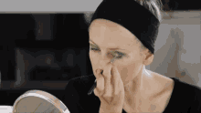 a woman wearing a black headband applying green eye shadow