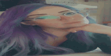 a woman with purple hair and glasses looks at the camera .