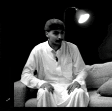 a man in a white robe is sitting on a couch under a lamp