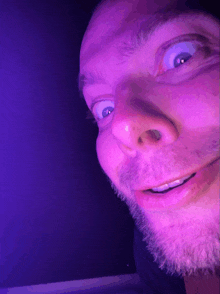 a close up of a man 's face with a purple light behind him