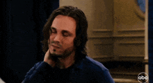 a man with long hair and a beard looks at the camera with a abc logo behind him