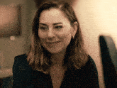 a woman in a black shirt and earrings smiles for the camera