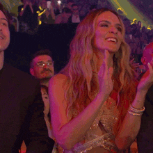 a woman in a gold dress is clapping her hands in front of a crowd