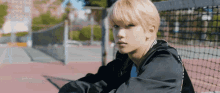 a young man with blonde hair is sitting on a tennis court .