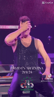 a man in a black tank top is covering his face with his hand .