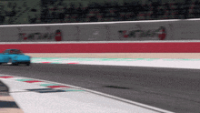 a blue car is driving down a race track with the word tchai on the wall