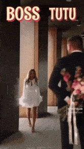 a woman in a white dress is walking towards a man in a suit holding flowers ..