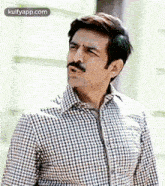 a man with a mustache is wearing a plaid shirt and looking at the camera .