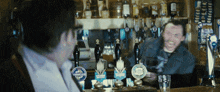 a man sitting at a bar talking to another man with a beer tap that says ' guinness ' on it