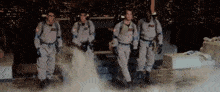a group of ghostbusters are walking through a foggy room .