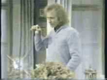a man in a blue sweater is standing in front of a window holding a flower .