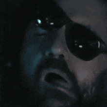a man with a beard wearing sunglasses looks at the camera
