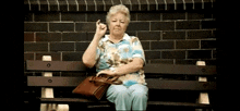 an elderly woman sits on a bench with a purse and a cigarette in her hand