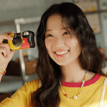 a woman in a yellow shirt is smiling and holding a kodak camera