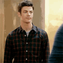 a man in a plaid shirt is standing in front of a wall and looking at another man .