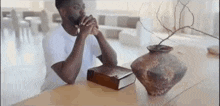 a man is sitting at a table with his hands folded and a bible on it .
