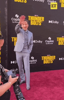a man in a suit is standing on a red carpet with thunder bolts written on it
