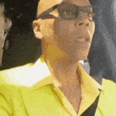 a bald man wearing glasses and a yellow shirt is sitting in a car .
