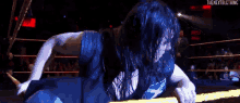a wrestler is laying on the ground in a wrestling ring while a crowd watches .