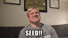 a man sitting on a couch with the words seed written on his shirt