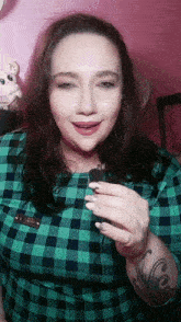 a woman wearing a green plaid shirt has a tattoo on her arm that says " co "