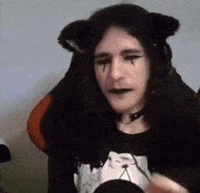 a man wearing cat ears and a choker is sitting in a chair and making a funny face .