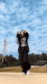 a woman in a black sweatshirt and black pants is dancing in front of a cloudy sky .