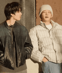 two men standing next to each other one wearing a leather jacket