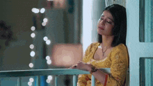 a woman in a yellow dress is sitting on a balcony looking out the window .