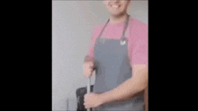 a man in an apron is cleaning a microwave with a sponge and smiling .