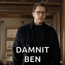 a man wearing glasses and a black jacket is standing in a hallway and says `` damnit ben '' .
